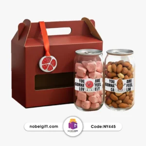 ست هدیه یلدایی NY445 شامل دو شیشه آجیل و شیرینی با برچسب‌های انگیزشی و آویز انار در جعبه قرمز.